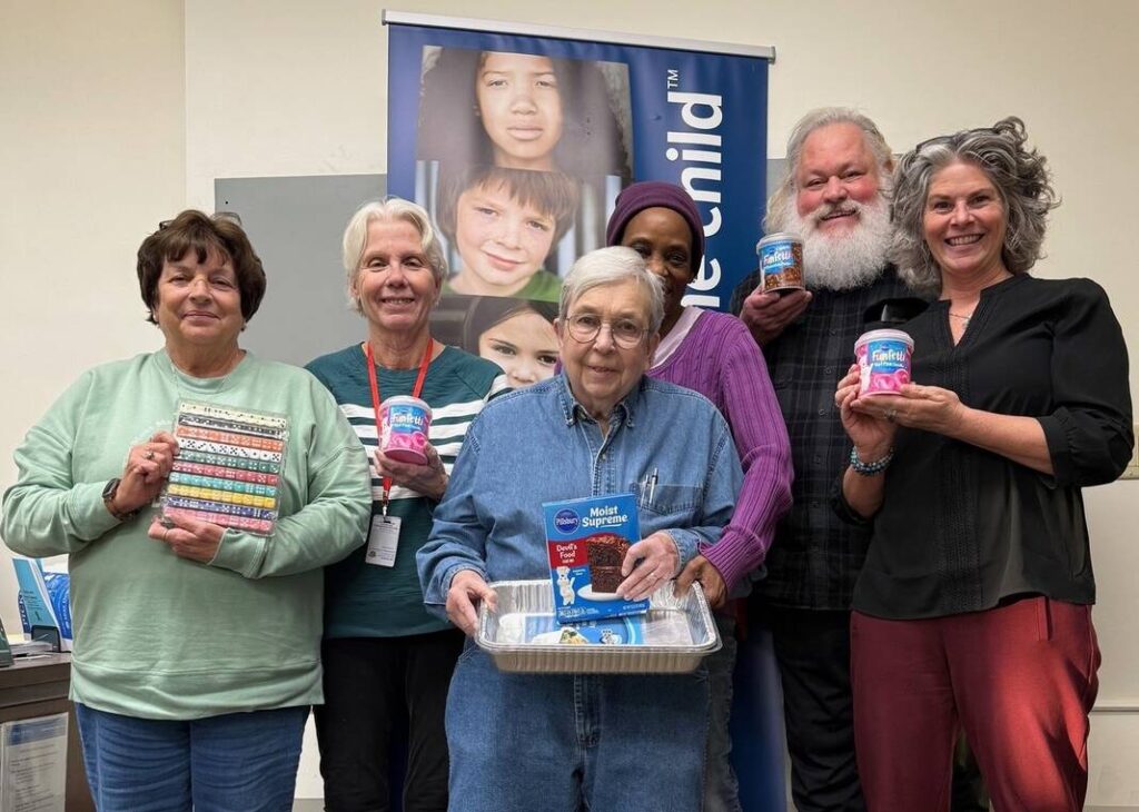 A group of people posing in a room, holding items used to make cake.