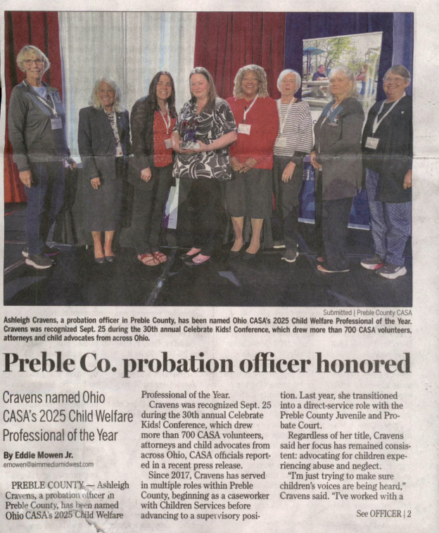 A newspaper clipping showing a group of people on stage, including a woman holding an award.